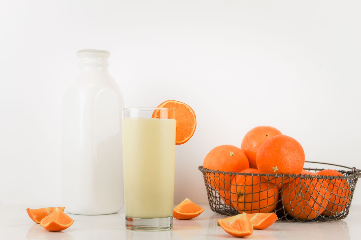 on a table sits a jug of milk, a basket of orange and a glass of kefir smoothie