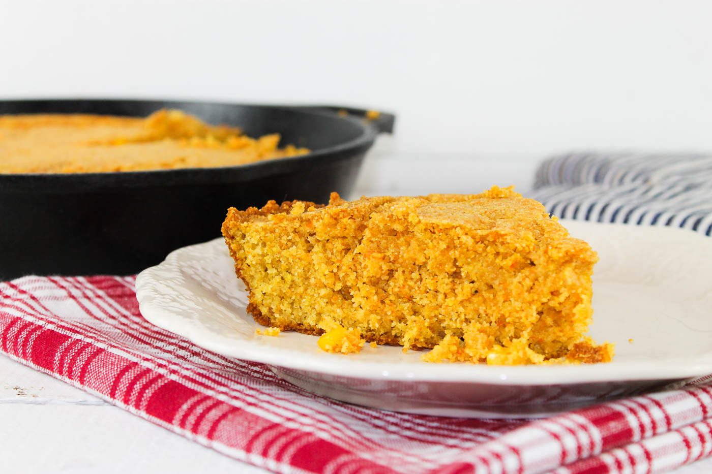 slice of cornbread sits on a plate in front of a lodge cast iron skillet
