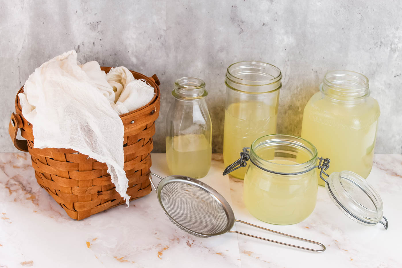 basket filled with cheesecloth sitting next to four jars filled with liquid whey