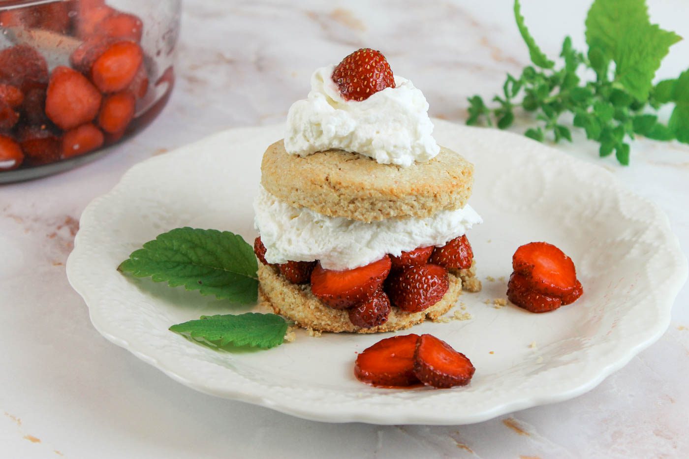 sliced berries, greenery, a bowl of strawberry sauce and a shortcake sit on a kitchen countertop