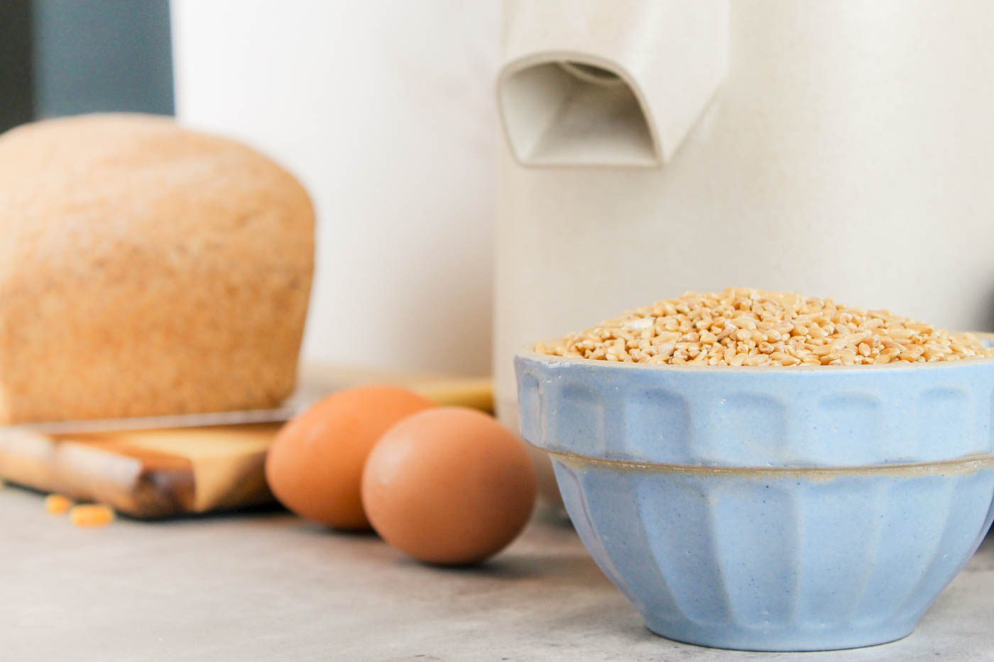 a bowl of wheat berries sitting in front of eggs and a mockmill grain mill