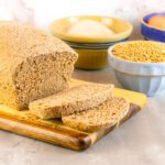 loaf of sandwich bread sits on a cutting board beside bowls of baking ingredients