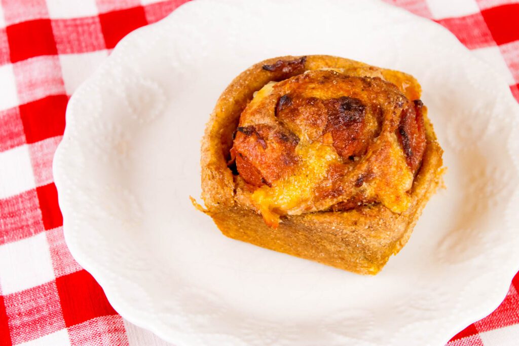 a single roll filled with meat and cheese sits on a white plate