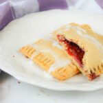 two toaster pastries sit on top of a cream colored plate next to a purple kitchen towel