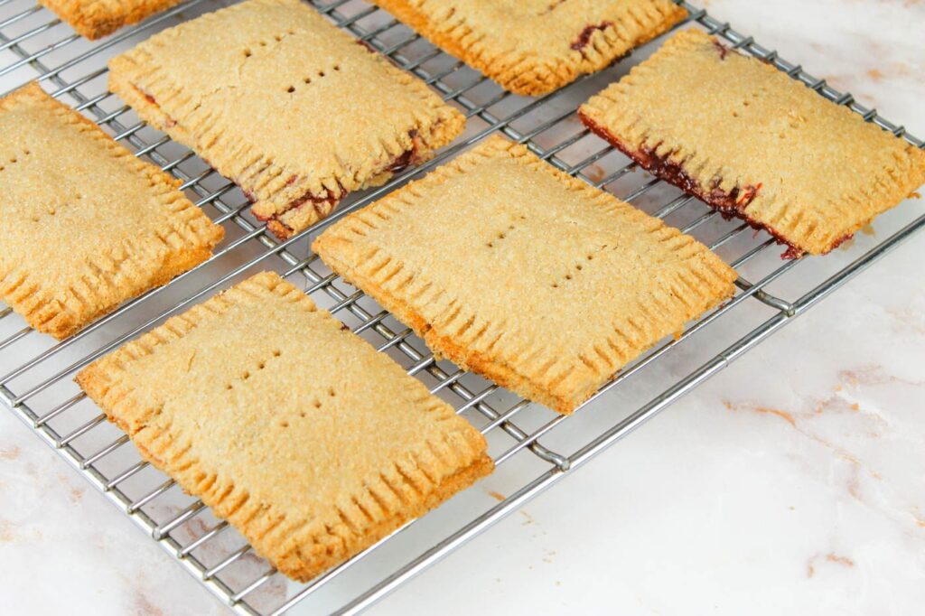 a bunch of jam filled pastries sit on a metal rack to cool from the oven