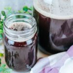 mason jar filled with elderberry soda sitting next to some greenery and a purple towel