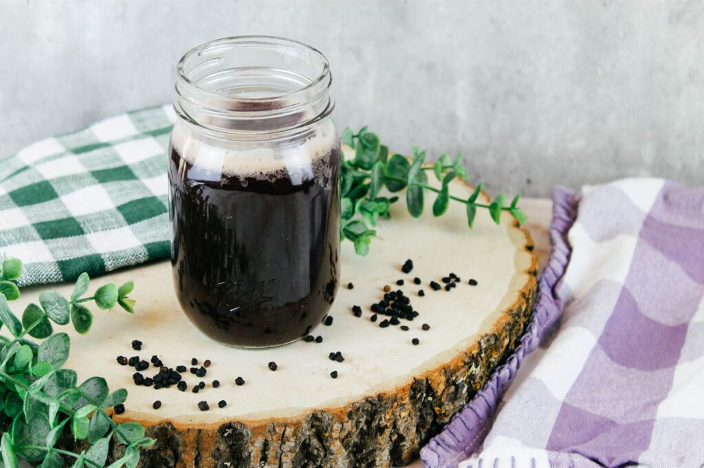 glass mason jar filled with soda sits on a slab of wood surrounded by greenery