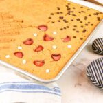 sheet pan pancakes with fresh milled flour sits on a countertop beside a wooden spatula, a tea towel and an oven mit