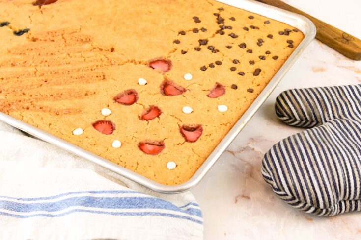 sheet pan pancakes with fresh milled flour sits on a countertop beside a wooden spatula, a tea towel and an oven mit