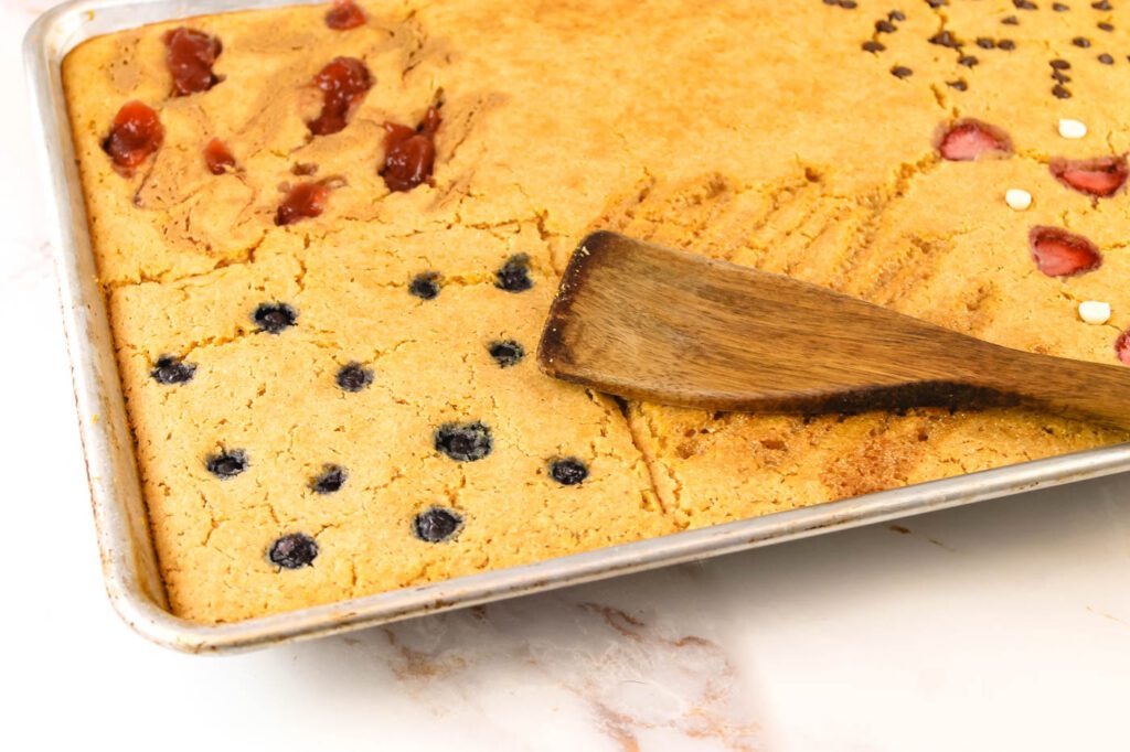 a wooden spatula lays atop a baking pan with pancakes