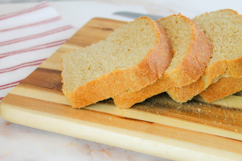 a stack of sliced bread laying across a wooden cutting board and a striped tea towel
