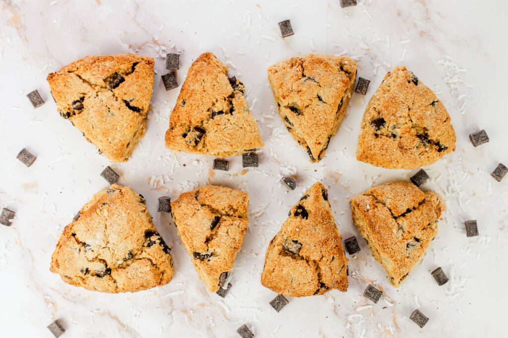 eight scones sitting on a marble countertop with bits of chocolate and coconut sprinkled around each piece