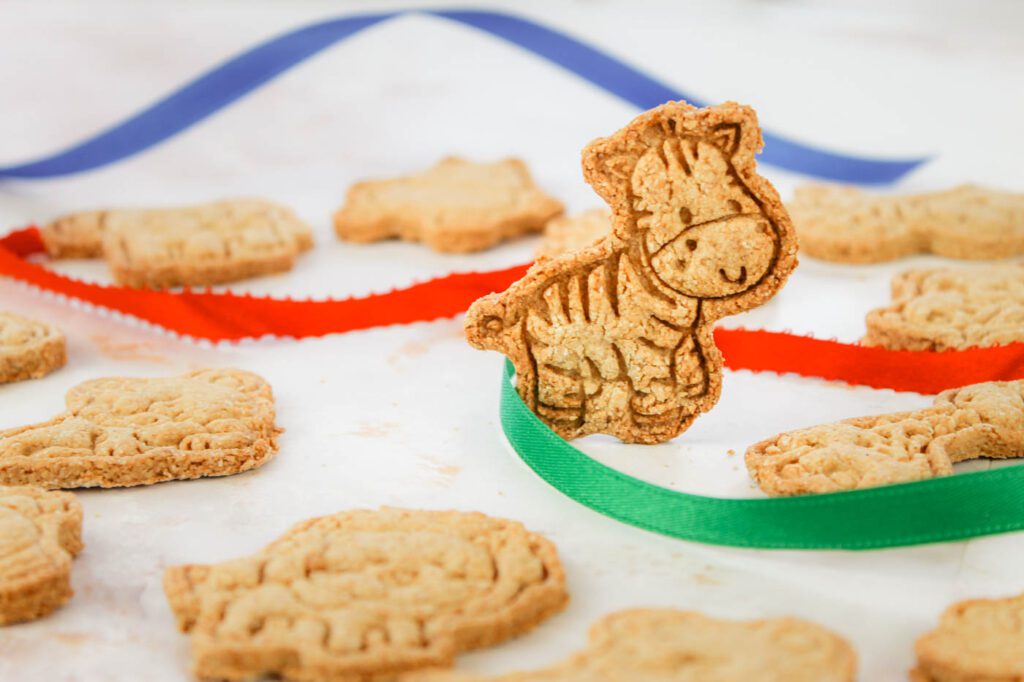 a zebra shaped cookie is standing next to more cookies and some colored strands of ribbon