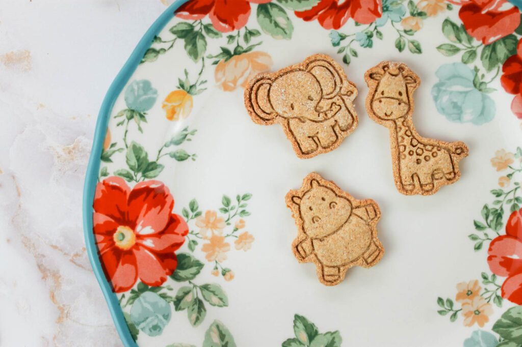 a hippo, giraffe and elephant shaped animal cracker lay on a floral plate in the kitchen
