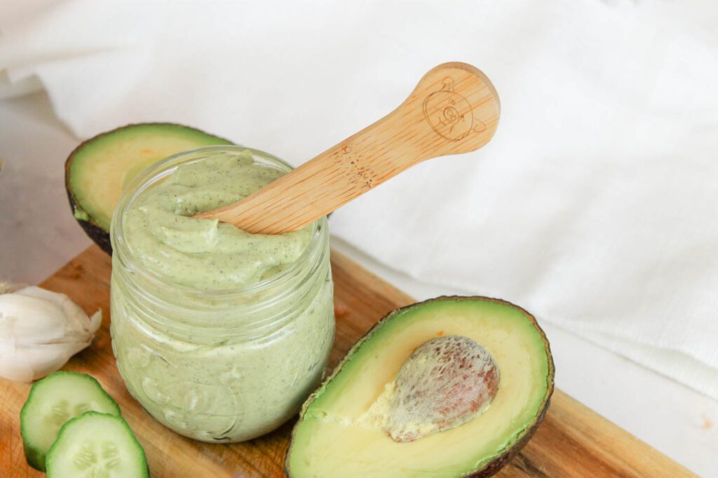 jar of kefir dressing with a wooden spoon stuck in the top. jar sits besides a bunch of sliced veggies including an avocado