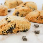 chocolate coconut scone with fresh milled flour sitting on a countertop surrounded by shreds of coconut and pieces of chocolate