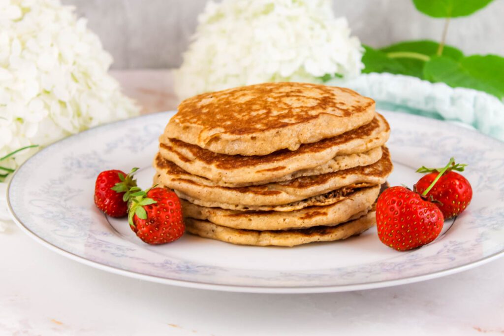 stack of pancakes with kefir on a plate beside 4 strawberries