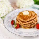 stack of kefir pancakes sits on a floral plate beside fresh berries and flowers