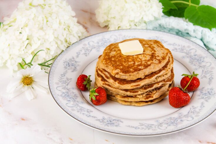 stack of kefir pancakes sits on a floral plate beside fresh berries and flowers