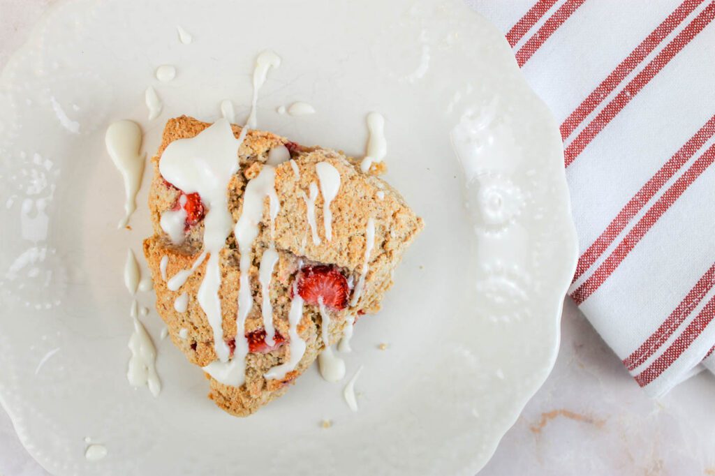 small white glass plate with a strawberry scone covered in a vanilla glaze