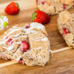 strawberry and cream scones sitting on a wooden cutting board surrounded by berries and flowers