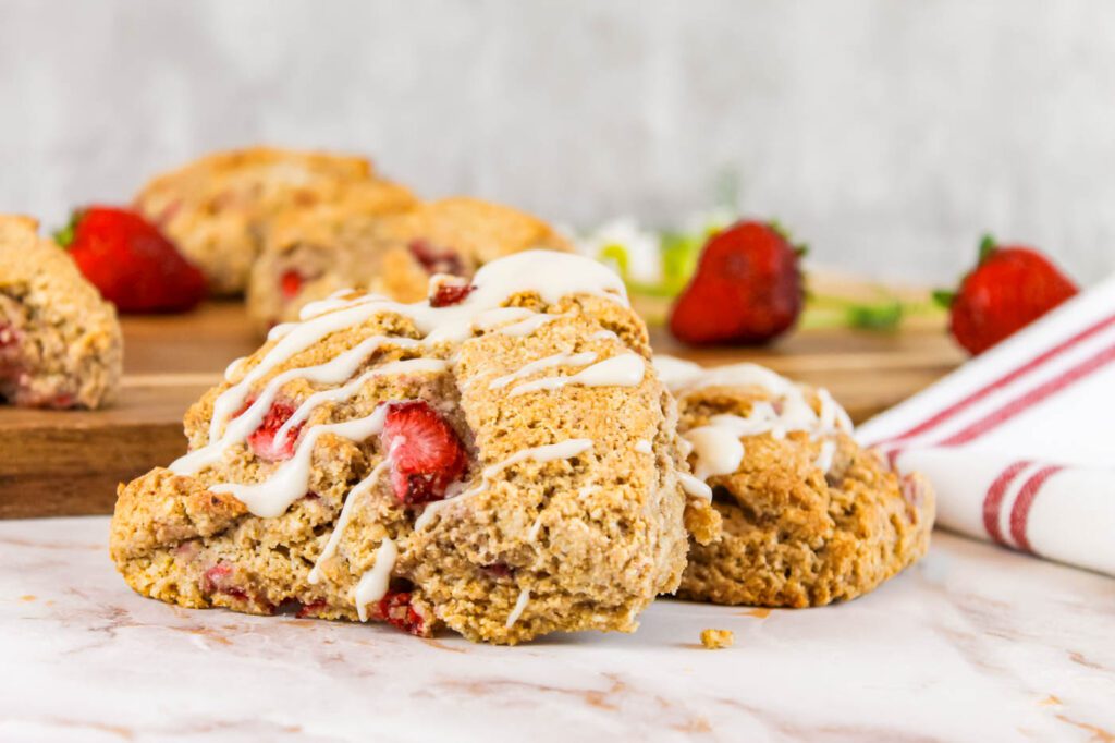 two scones stacked on top of each other. strawberries and a striped tea towel sit int he background.