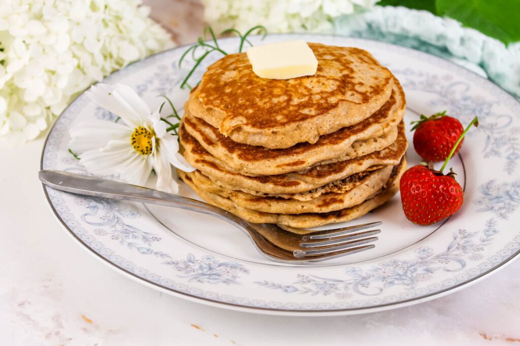 four pancakes on a blue and white plate next to some white flowers and some fresh cut flowers