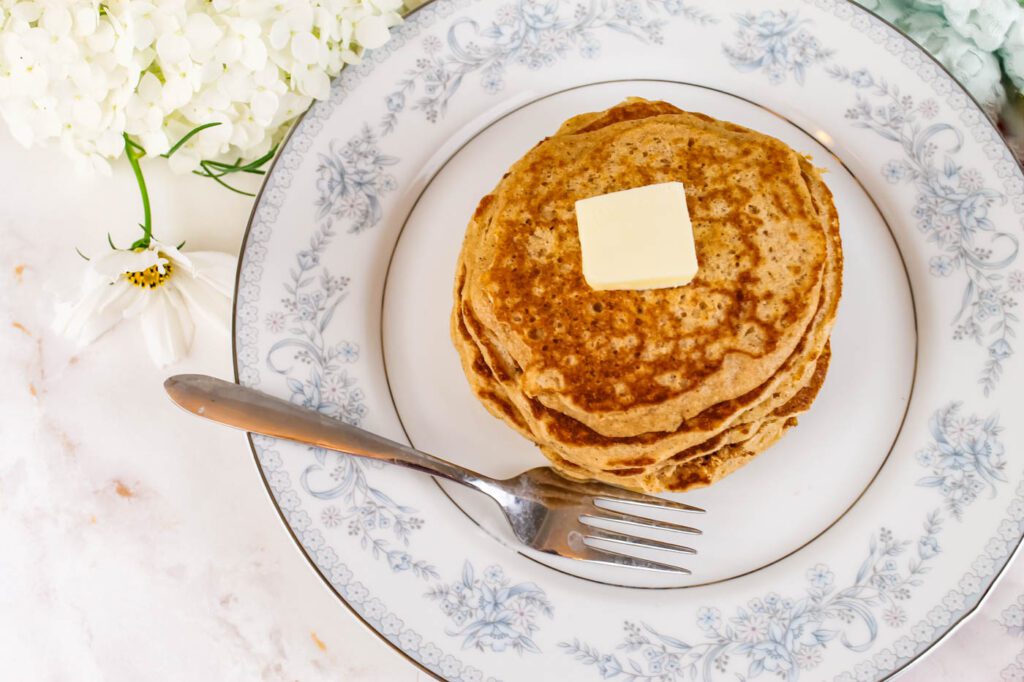 top down view of pancakes on a plate next to a silver fork and some white flowers