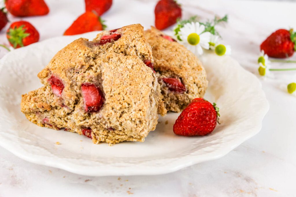 two strawberry scones sit on a white plate beside some chamomile flowers