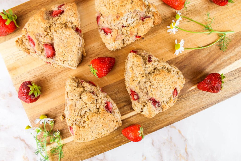 4 scones sit scattered across a cutting board with berries and flowers