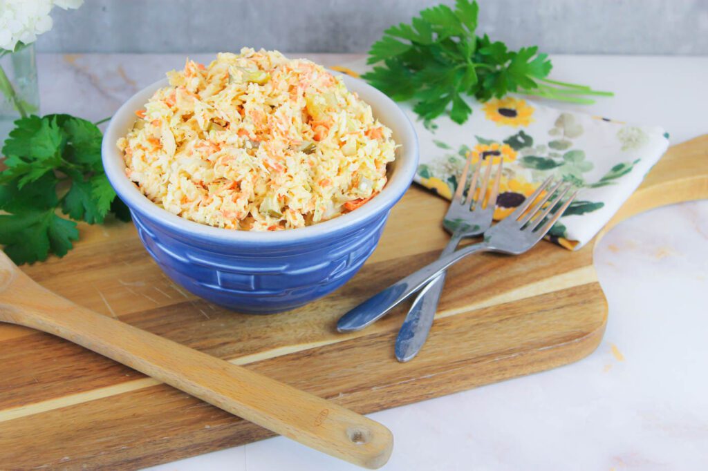 wooden cutting board with spoons, forks and a bowl of slaw on top