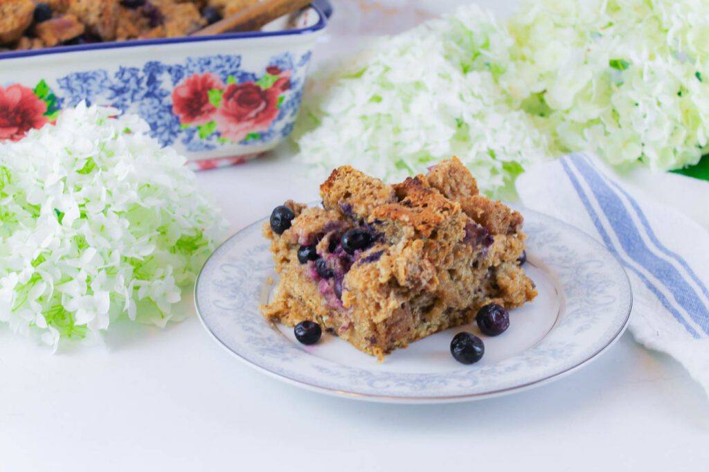 piece of french toast casserole with fresh milled bread sitting on a white and blue floral plate amongst some fresh cut flower