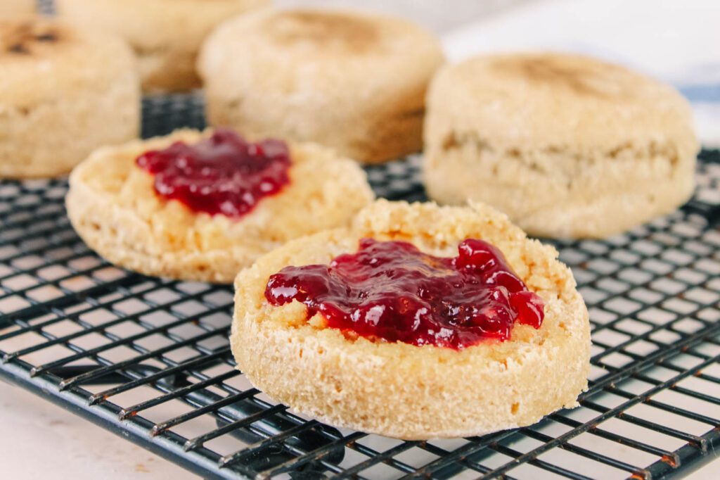 jam covered english muffins sit on a black cooling rack
