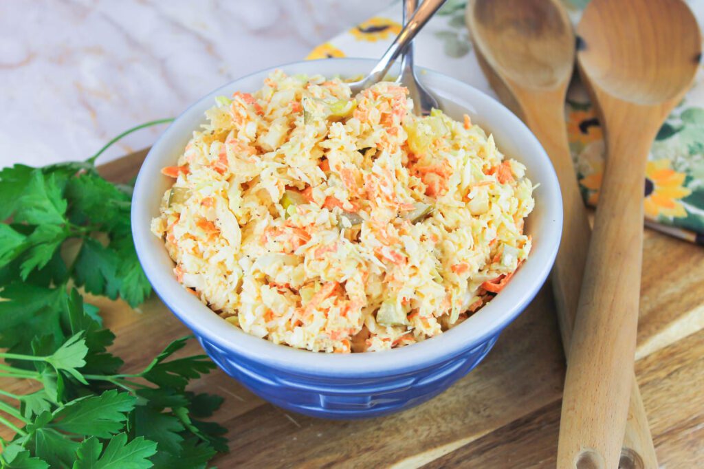 top down view of a bowl of slaw. two serving forks and some wooden spoons sit near the bowl.