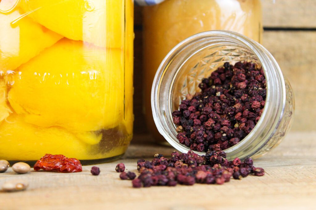 dried elderberries pouring out of a glass jar onto a wooden surface