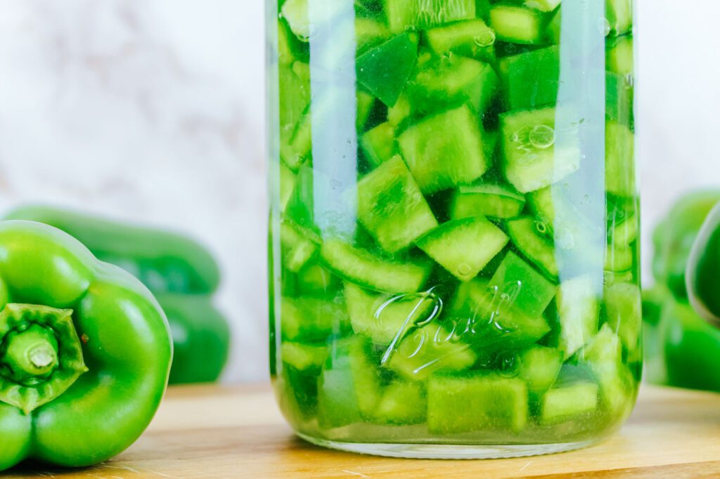jar of fermented green peppers surrounded by fresh peppers from the garden