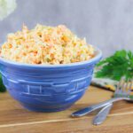 a small bowl bowl filled with creamy and tangy mustard coleslaw recipe sits on a wooden cutting board beside some forks and herbs