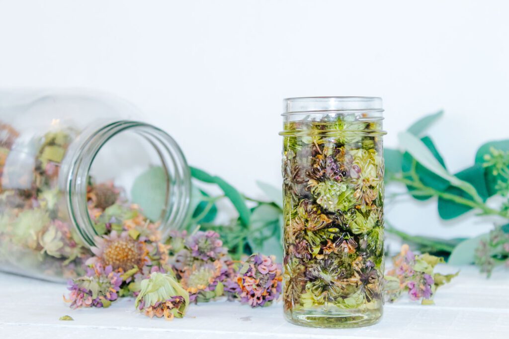 jar of herbs infused into oil sitting beside a jars of dried flowers