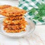 stack of zucchini fritters recipe with fresh milled flour sitting beside a green kitchen towel and fresh herbs