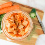 jar of fermented curtido recipe sitting on a cutting board surrounded by fresh herbs and vegetables