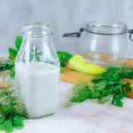 a bottle of kefir ranch dressing sitting beside fresh herbs, greens and a banana pepper