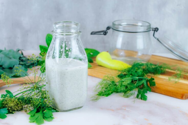 a bottle of kefir ranch dressing sitting beside fresh herbs, greens and a banana pepper