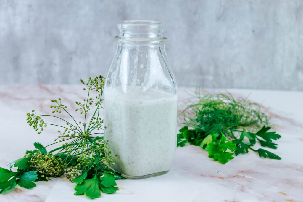 glass bottle of gut healthy salad dressing beside some dill and parsley