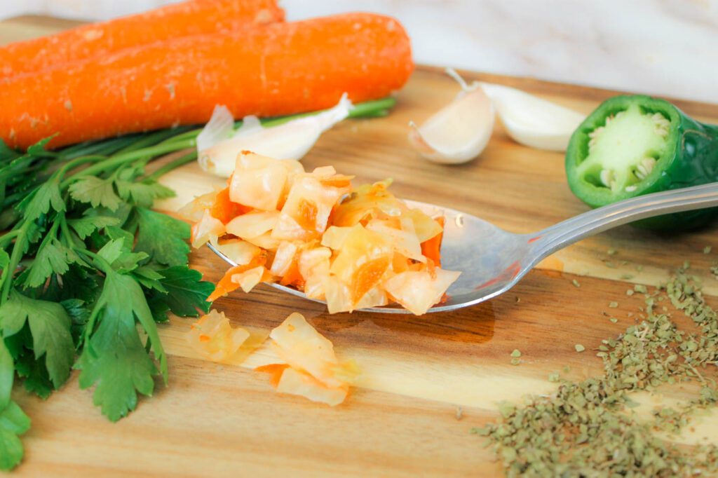 a spoon full of fermented curtido sits on a wooden surface surrounded by veggies and dried herbs