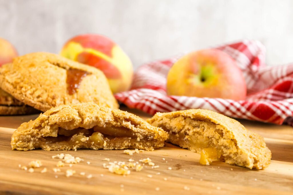 a divided apple hand pie sits on a wooden surface surrounded by fresh picked apples