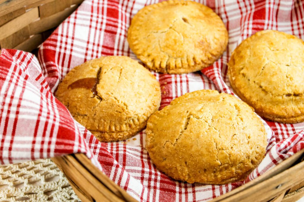 4 fruit filled hand pies sit in a wooden basket with a red plaid kitchen towel
