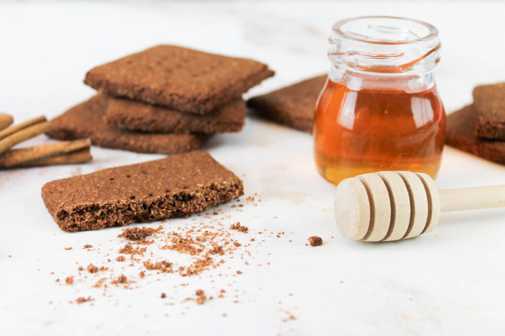 half eaten chocolate graham cracker on a marble countertop beside a jar of raw honey