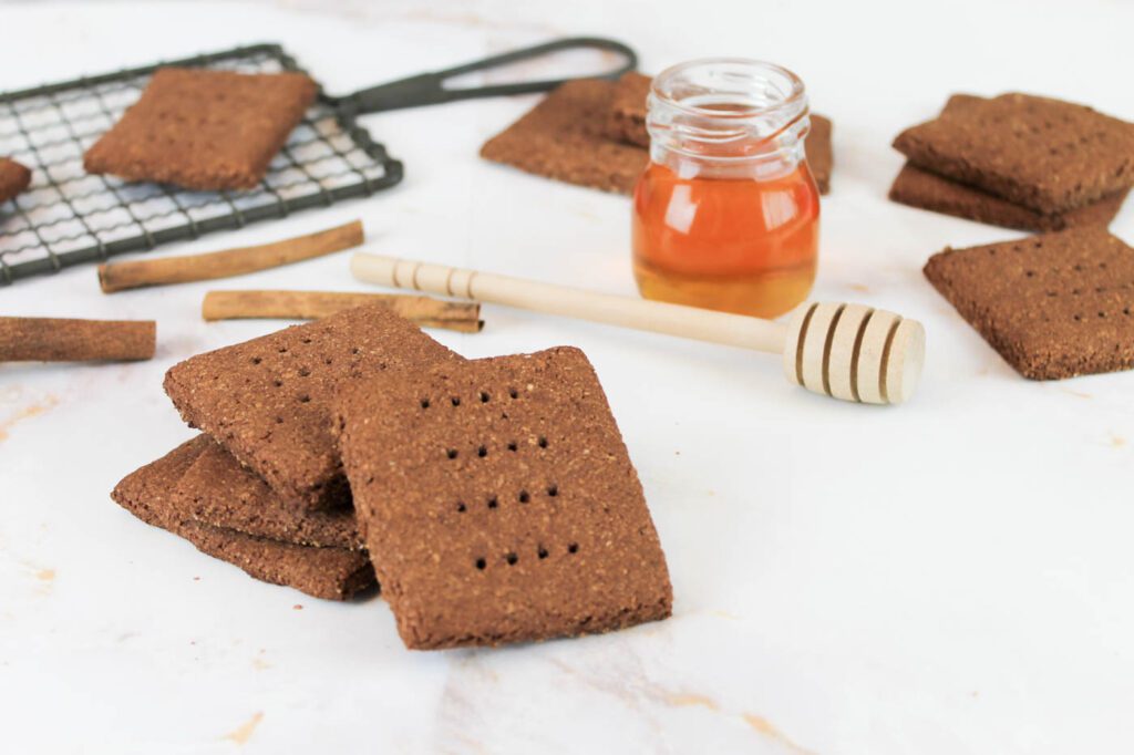 stack of chocolate crackers beside a jar of honey, a honey dipper and a black cooling rack