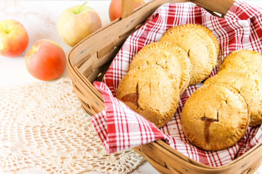 basket filled with apple hand pies next to a pile of fugi apples