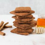 stack of healthy chocolate graham crackers sits beside cinnamon sticks and a jar of honey